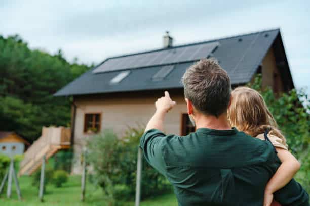 A man holding a child while pointing at residential rooftop solar panels..