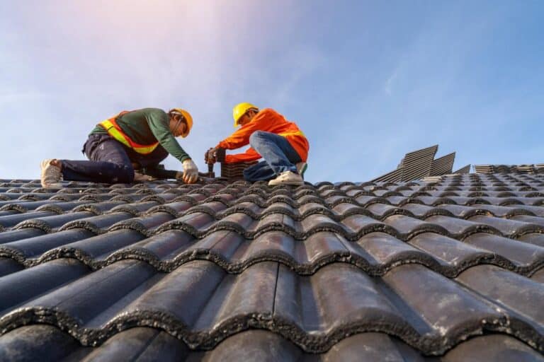 Two professional roofing contractors install dark tiles during a high-quality roof installation.